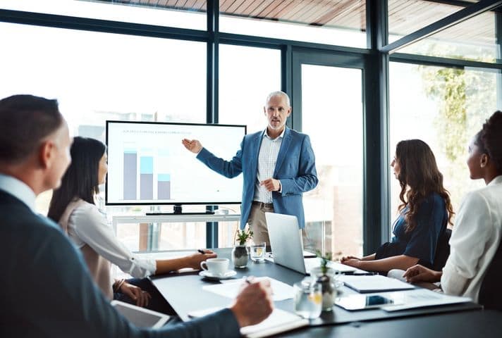 Man presenting bar charts on a screen in a bright windowed office