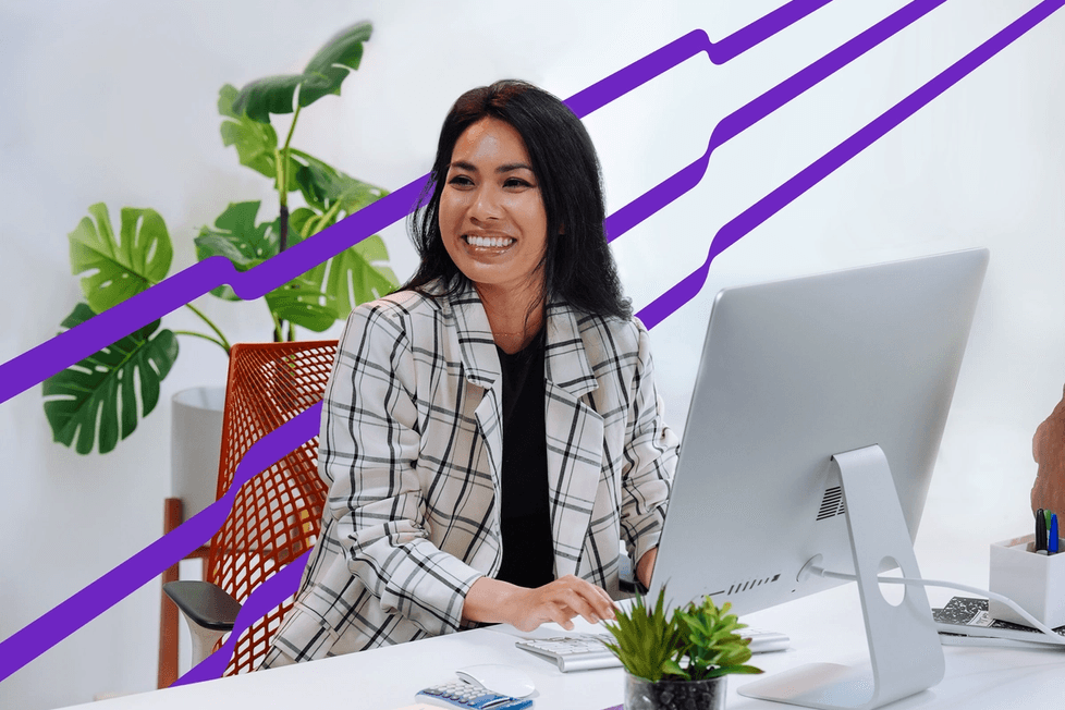 A woman sits at a desk, smiling while looking at a computer monitor. The desk features notepads, a pen, and a lush plant. Purple diagonal lines extend in the background.