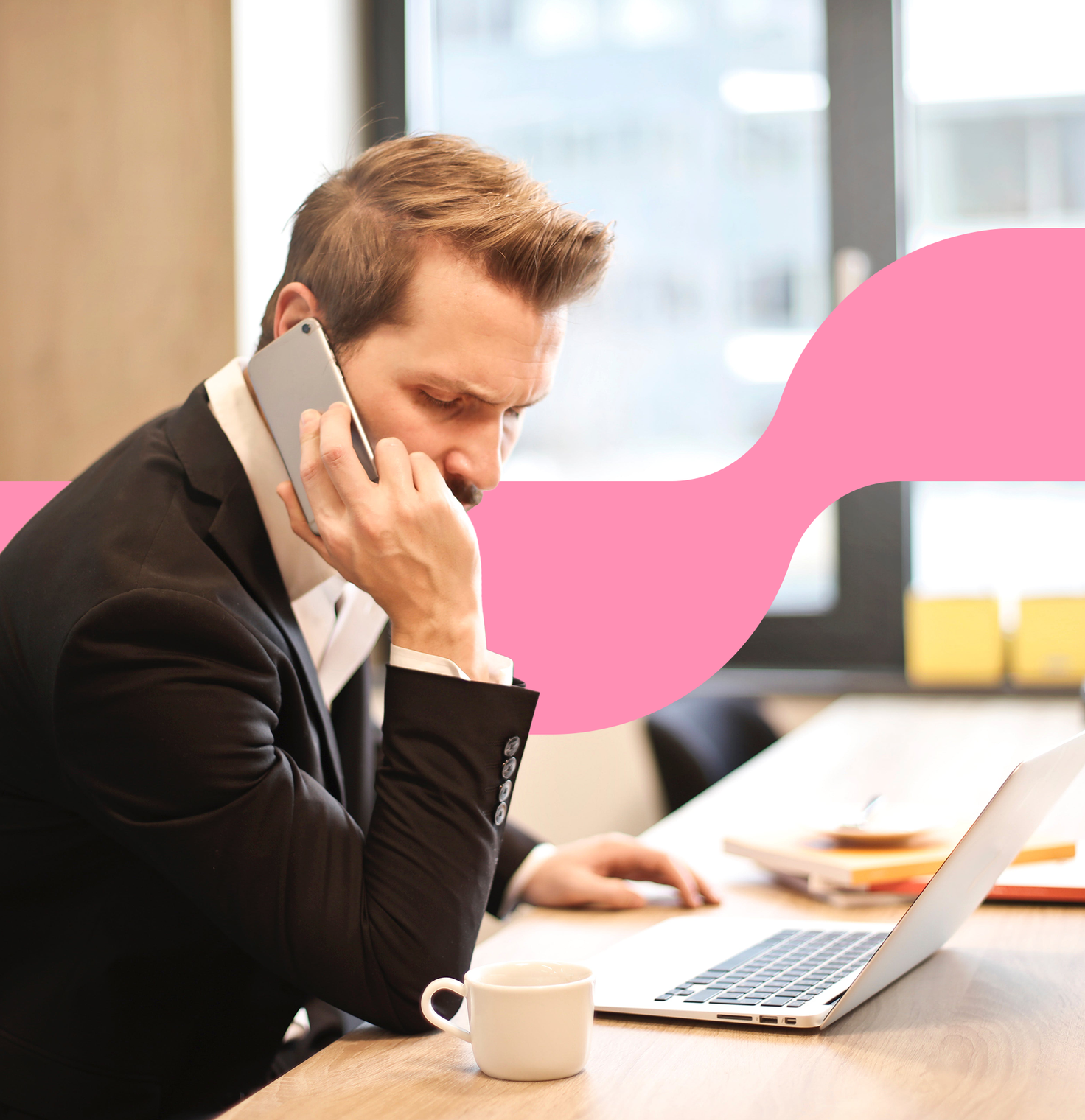Stock photo of a man in a black suit seated at a desk, holding a phone to his ear with a laptop and a cup of coffee in front of him. A pink wave design overlays part of the background.