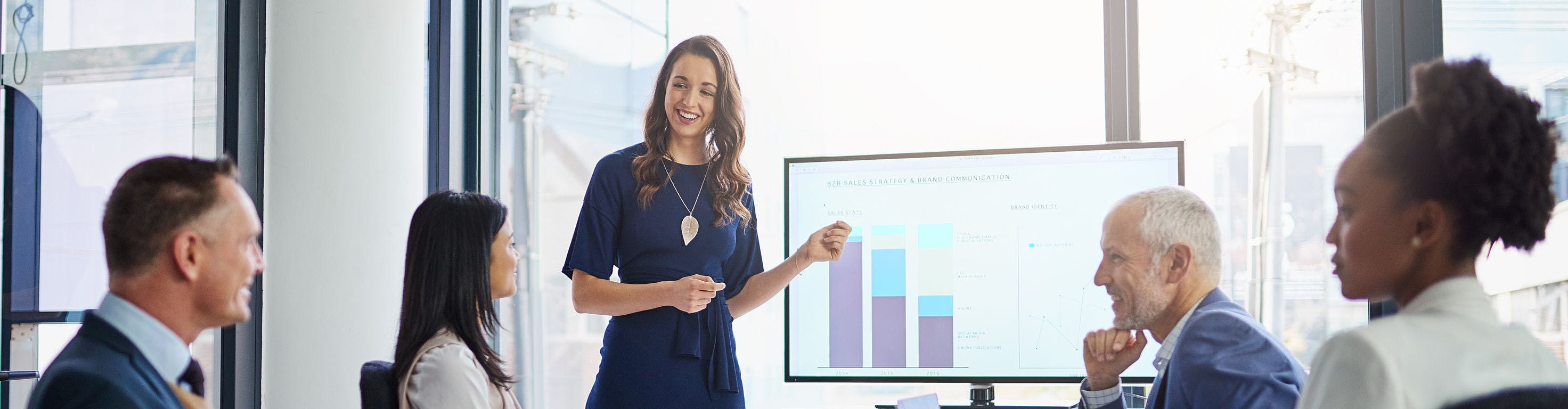 Woman presenting a bar chart graph on a screen in a bright windowed office