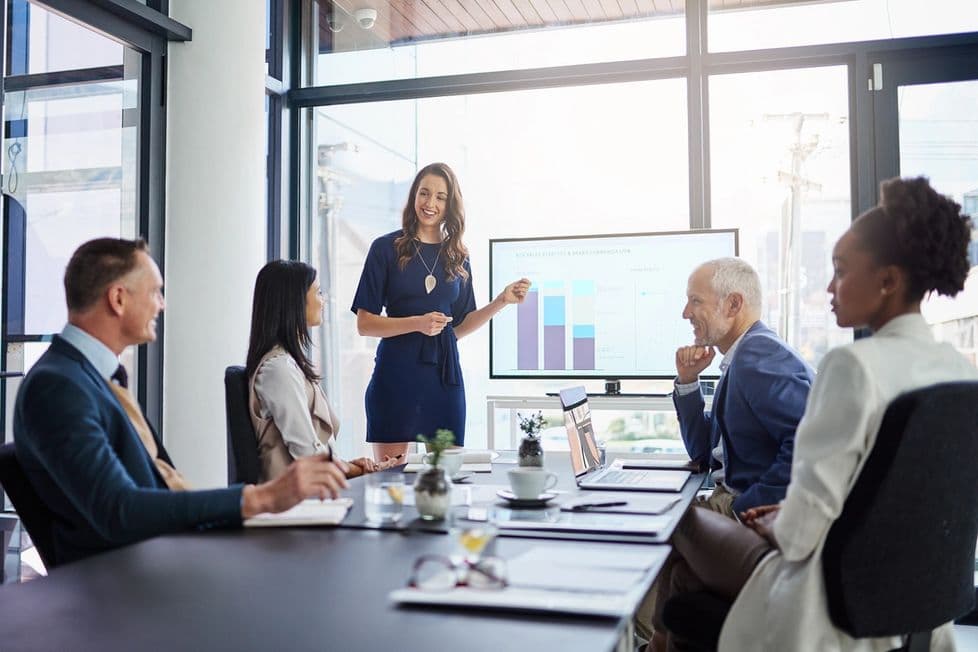 Woman presenting a bar chart graph on a screen in a bright windowed office