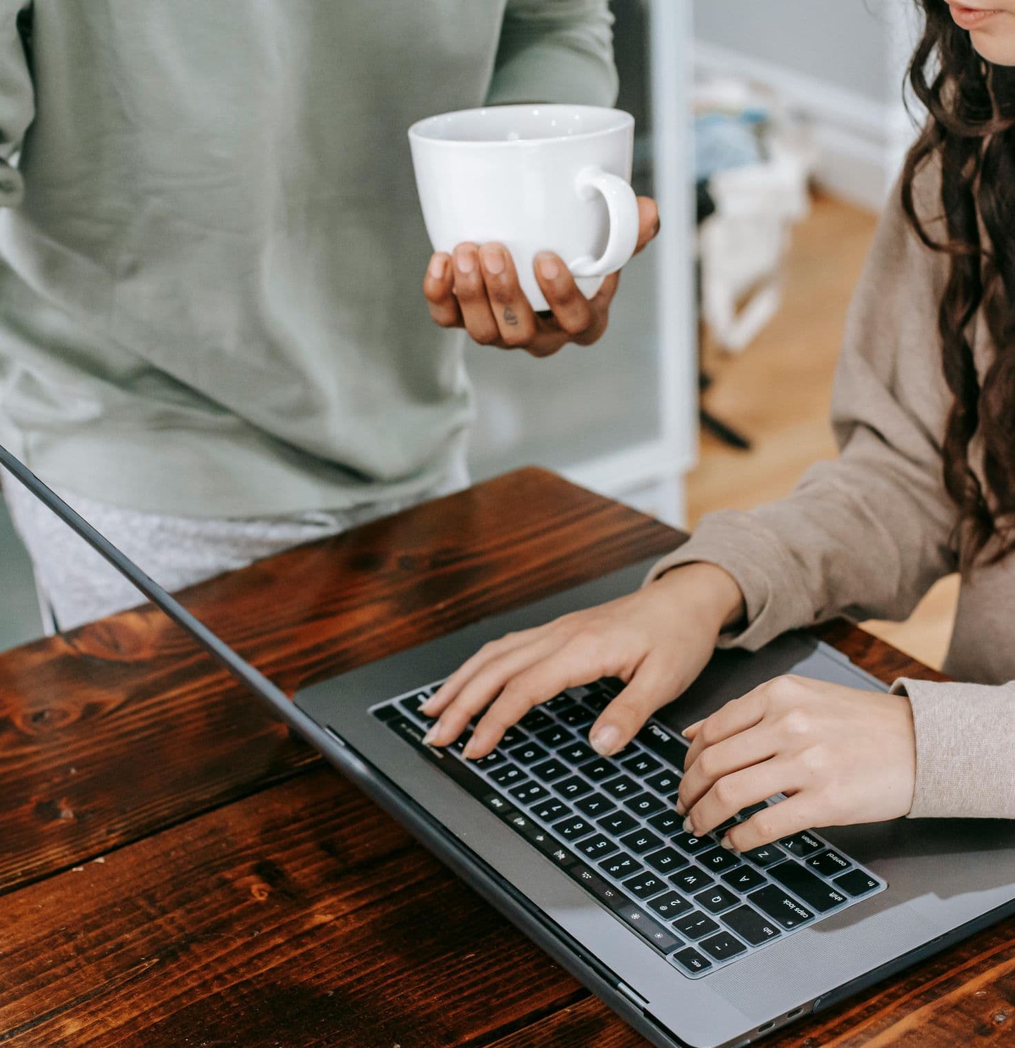 Close up of hands around a computer with a coffee cup