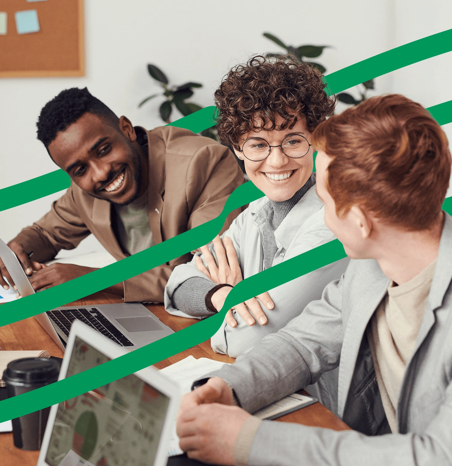 Stock photo of three people sitting at a wooden table in an office, engaged in a conversation with laptops and coffee in front of them. Green lines are extending across the picture.