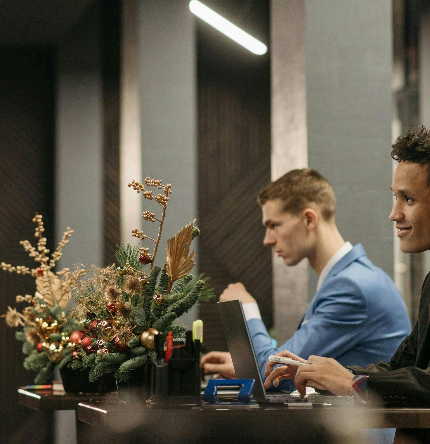 Two men working at a desk with a holiday floral arrangement