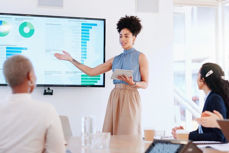 Woman presenting technical charts on a screen to a room full of women