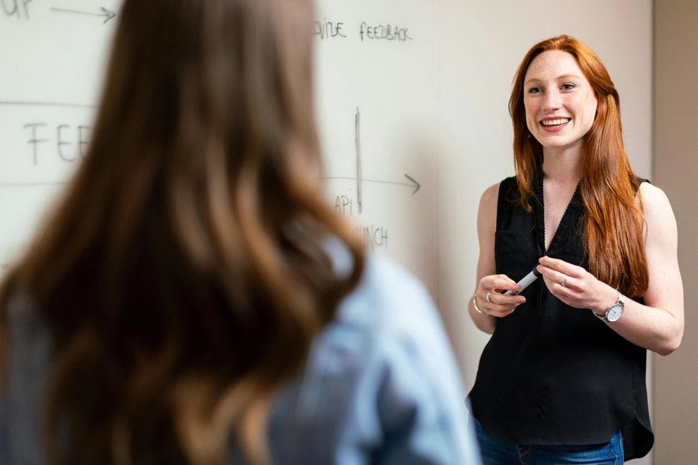 Woman standing at whiteboard talking to student or business person