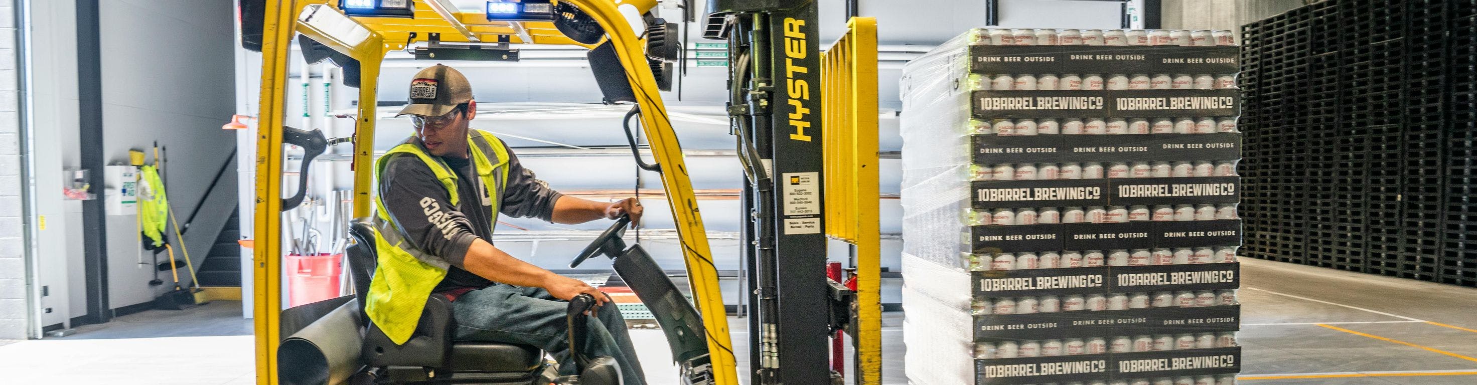 Man driving yellow forklift with a pallet full of cans in a warehouse