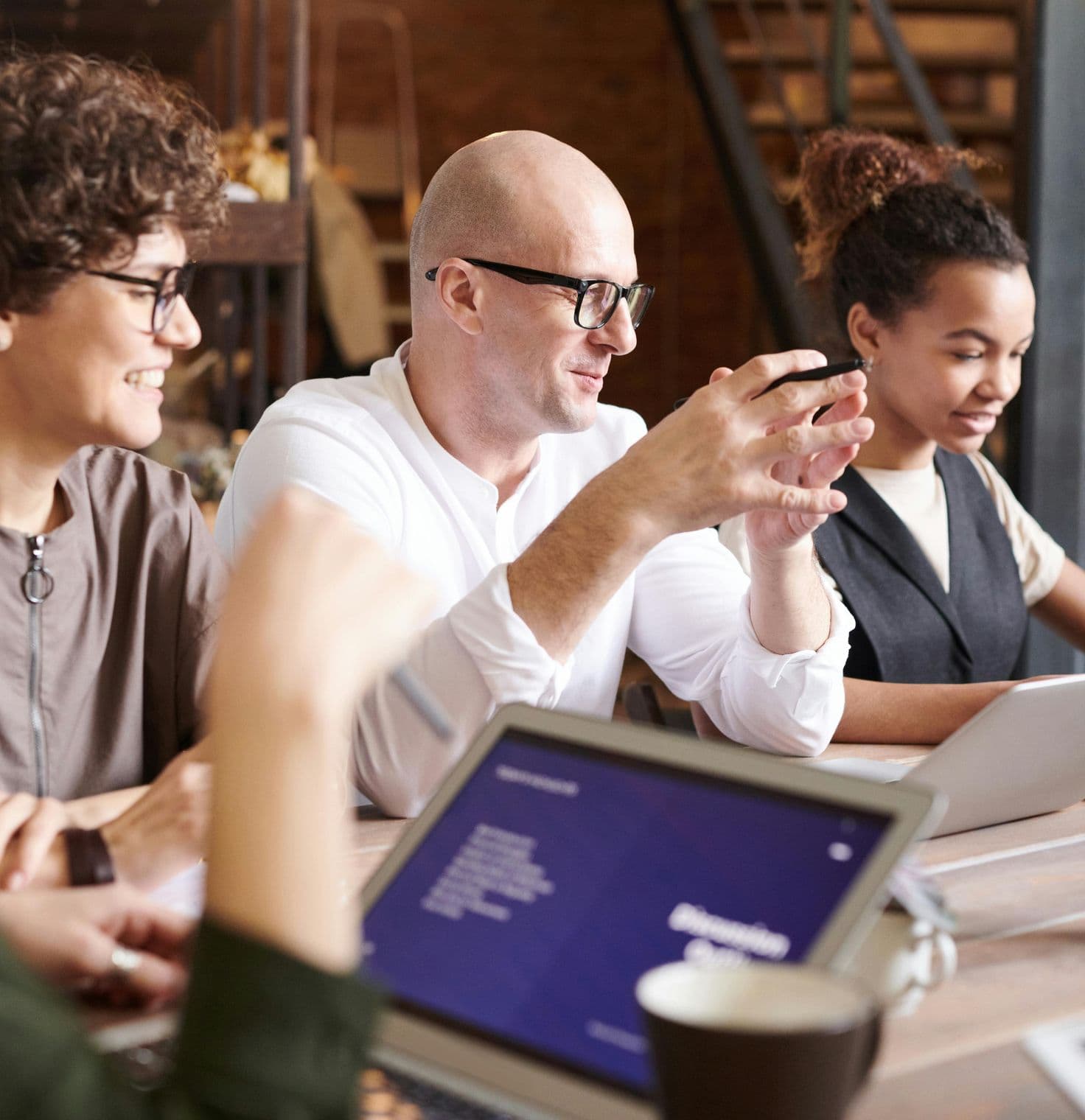 A diverse group of four people sits around a table, engaged in a discussion while working on laptops.